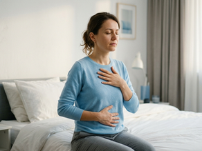 O femeie tânără practică respirația diafragmatică, ținând mâinile pe piept și abdomen pentru calmarea anxietății, într-un decor dormitor relaxant.