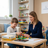 O psiholoagă blândă de la Clinica Blue realizează o evaluare psihologică pentru un copii, folosind jocul cu piese lego și teste standardizate precum WISC-V, în timp ce mama privește liniștită din fundal.