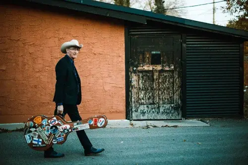 Picture of Tom Phillips walking on a street with a guitar case