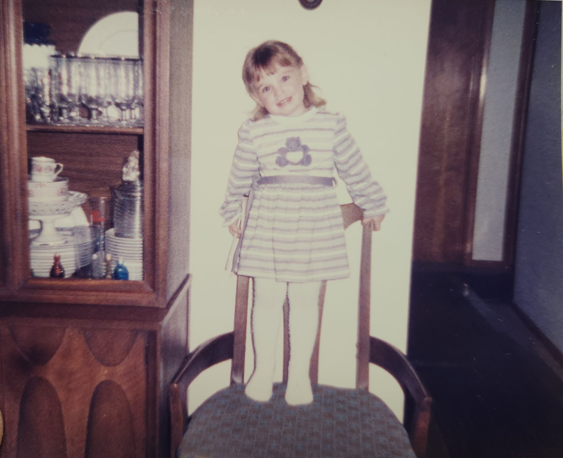 young girl standing on dining room chair next to hutch