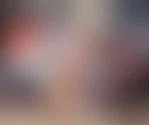 A group of smiling people sit on stairs, holding needlework in a cozy room. They wear colorful clothes, creating a warm, cheerful atmosphere.