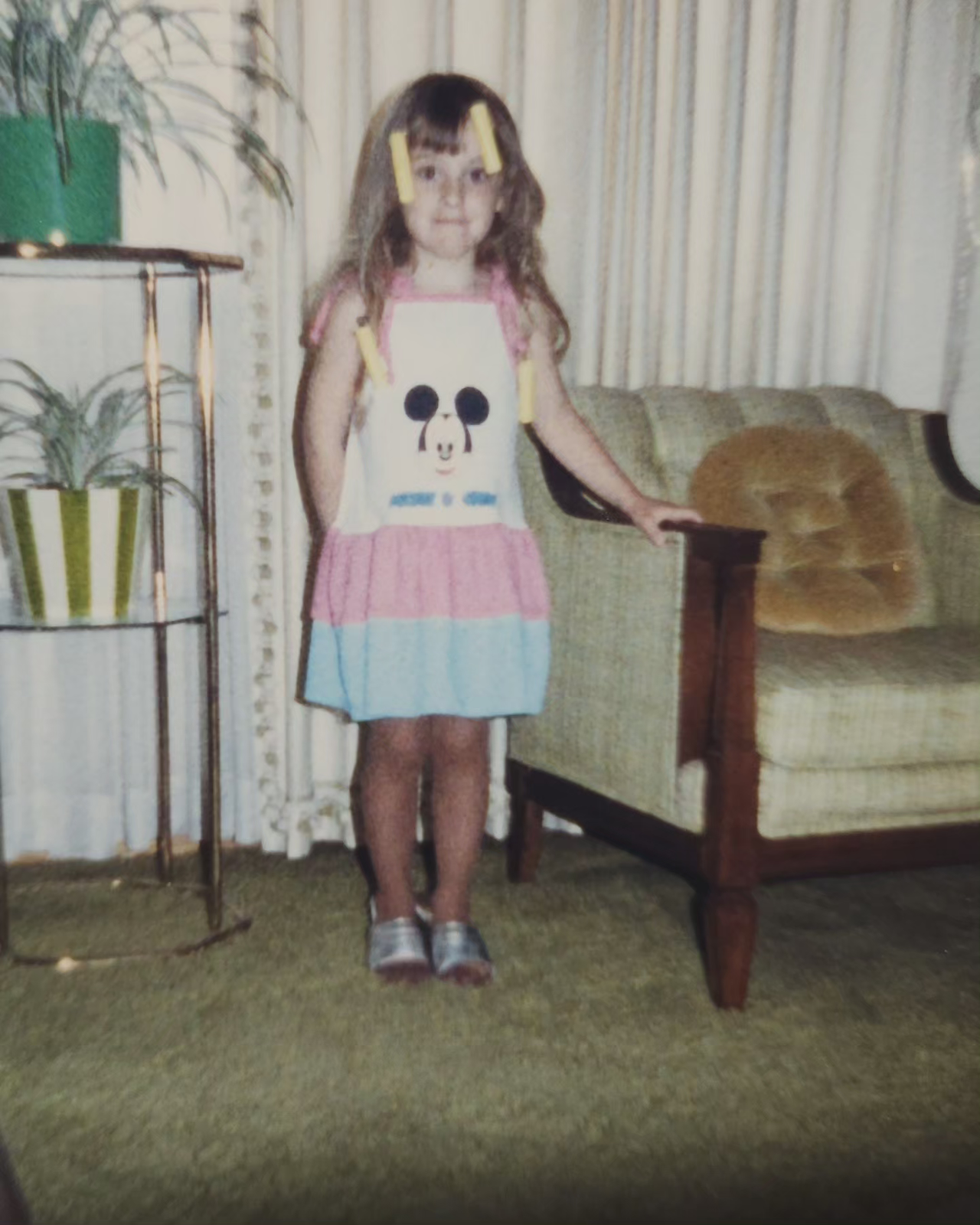 young child standing next to chair with plant stand next to her