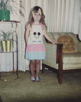 young child standing next to chair with plant stand next to her