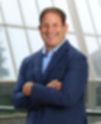Smiling man in blue suit, arms crossed, modern building background