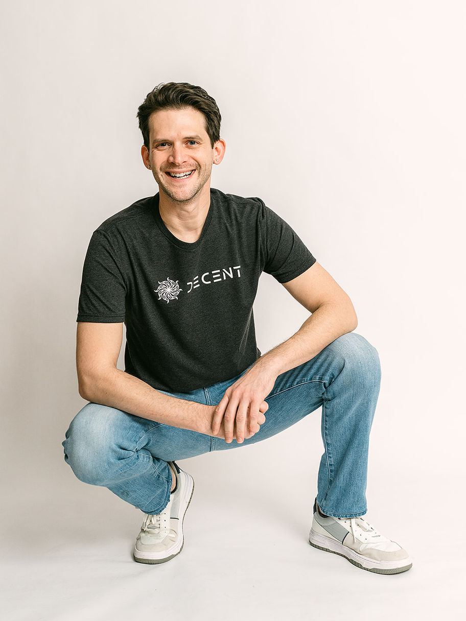 Smiling man crouching, wearing a black Decent Threads t-shirt