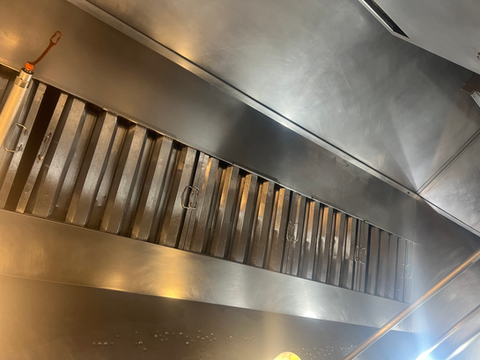 Stainless steel commercial kitchen exhaust hood with clean metal filters.