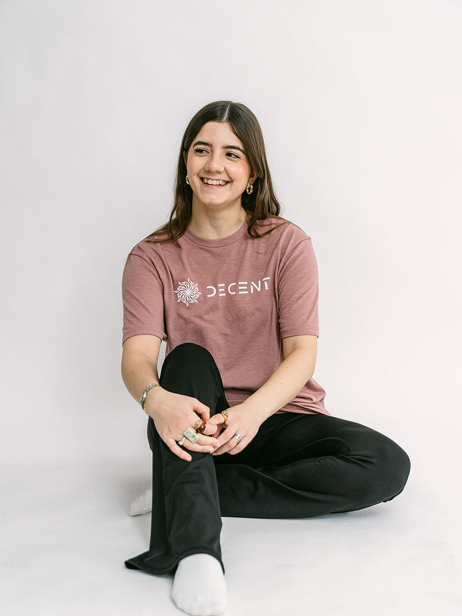 Smiling woman in a pink Decent Threads t-shirt and black pants, sitting