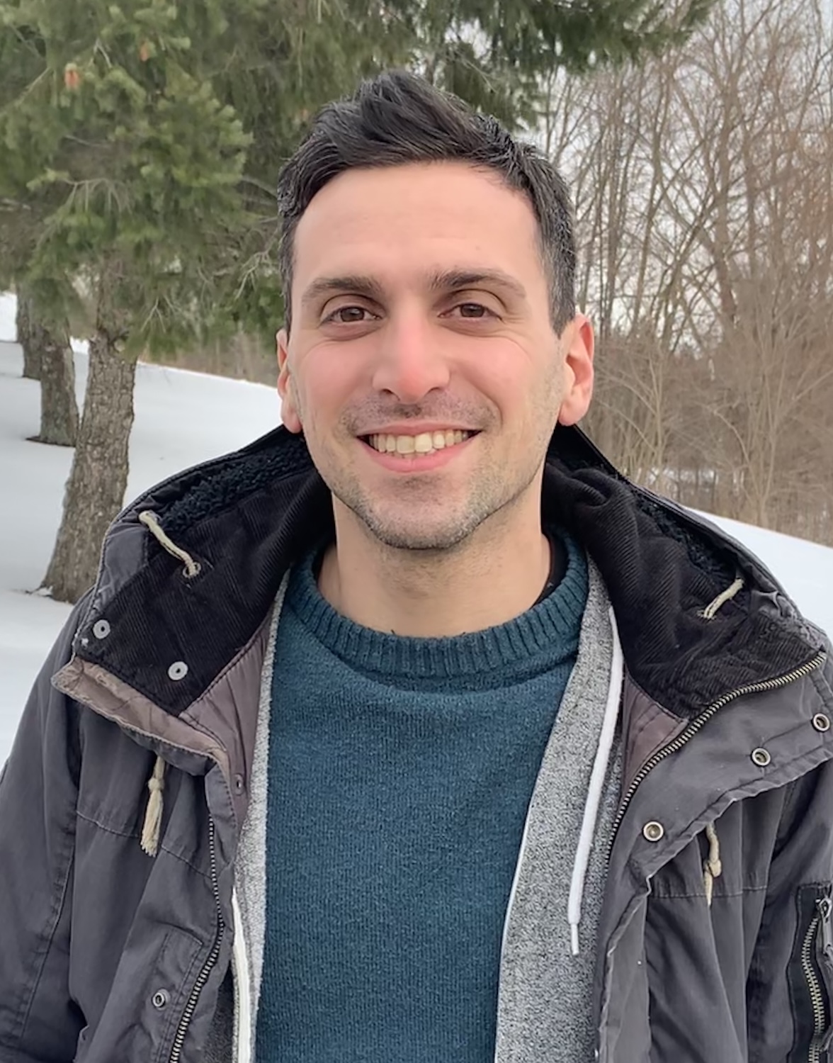 Smiling man in a winter jacket outdoors in the snow.