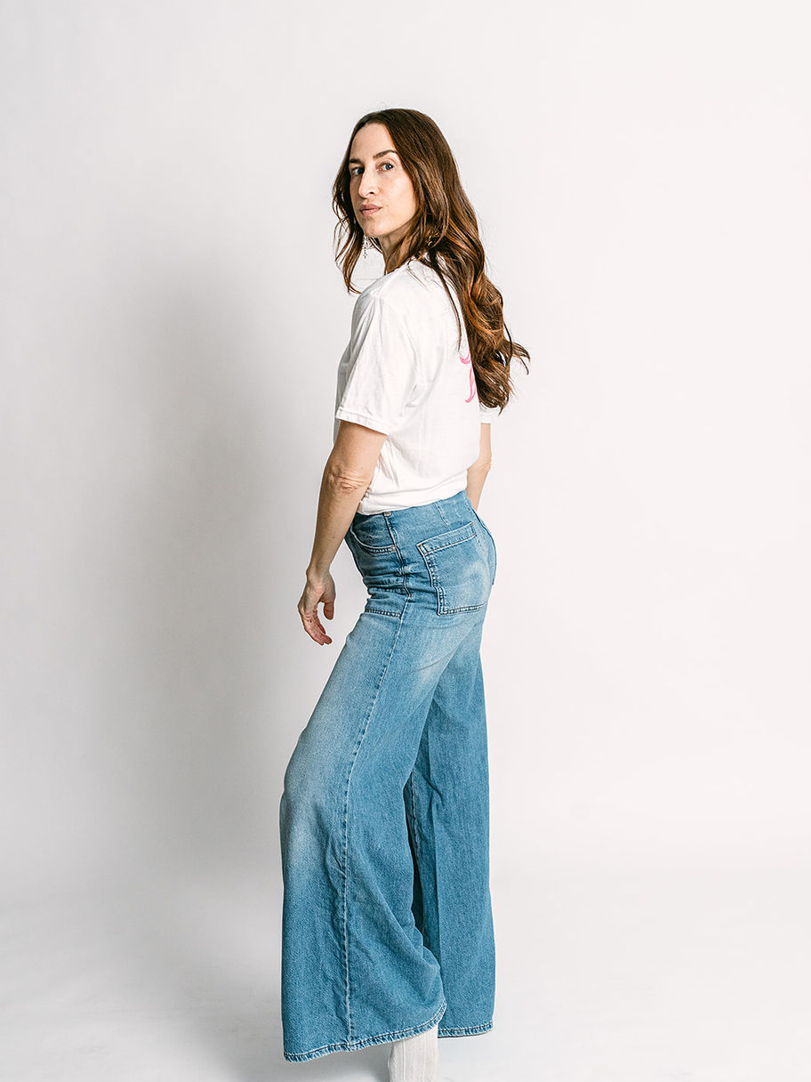 Woman in white Decent Threads t-shirt and wide-leg blue jeans, looking back