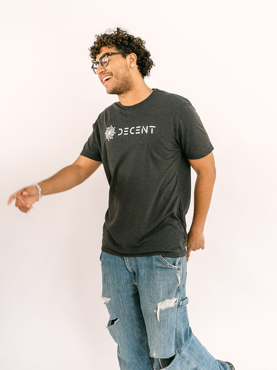 Smiling man in glasses, dark Decent Threads t-shirt, and jeans pointing