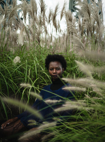 a woman in a blue sweater sits in a field of tall grass