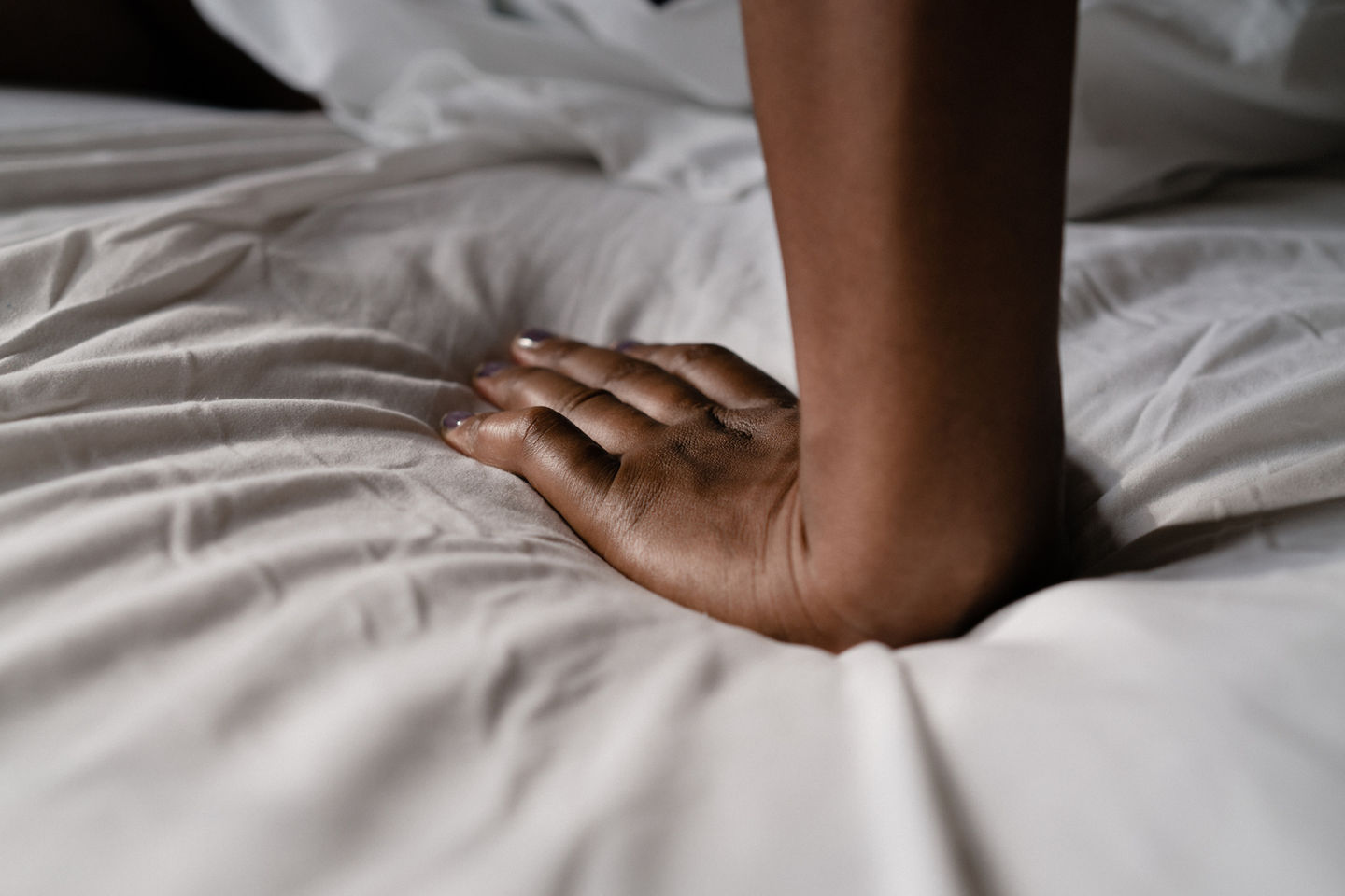 a woman 's hand rests on a bed with white sheets