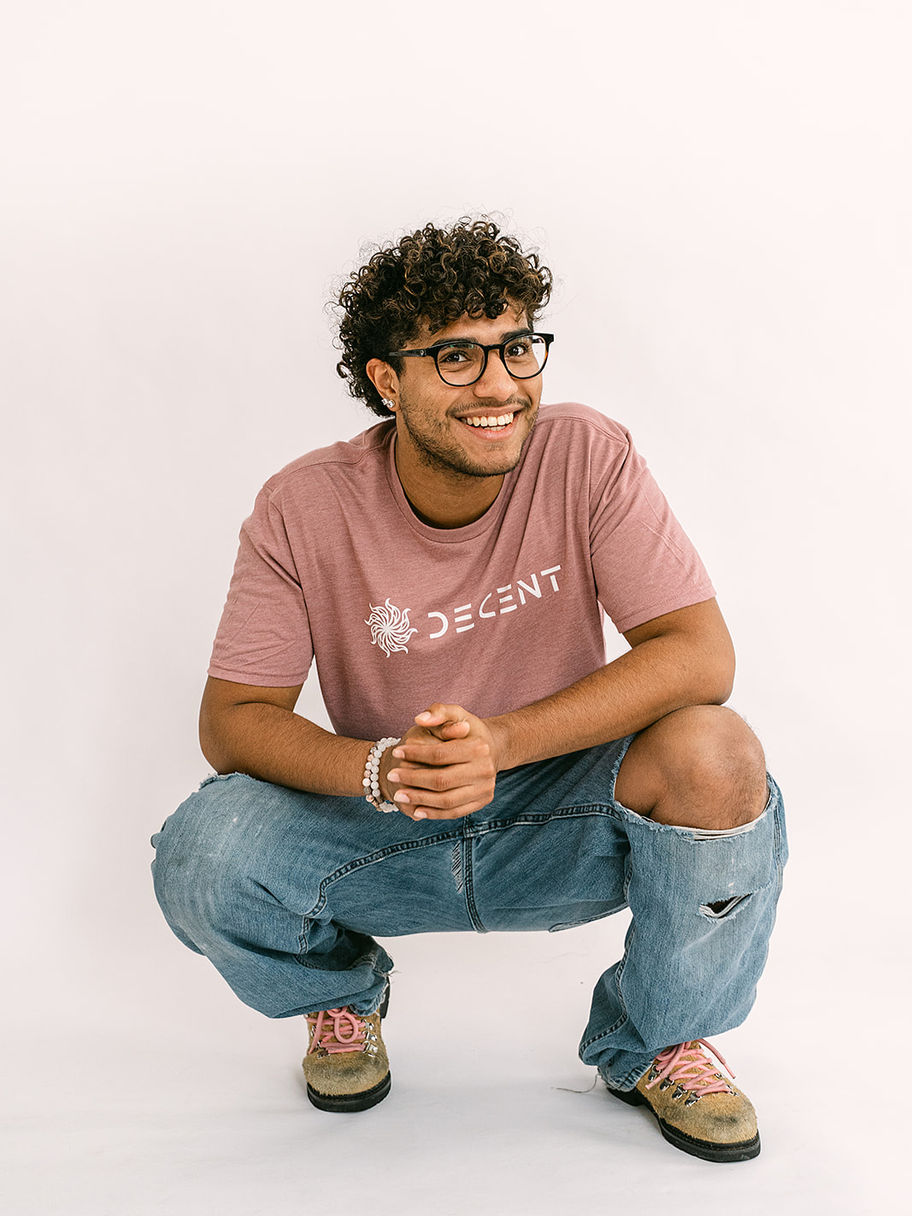 Smiling young man in a pink Decent Threads t-shirt and ripped jeans.