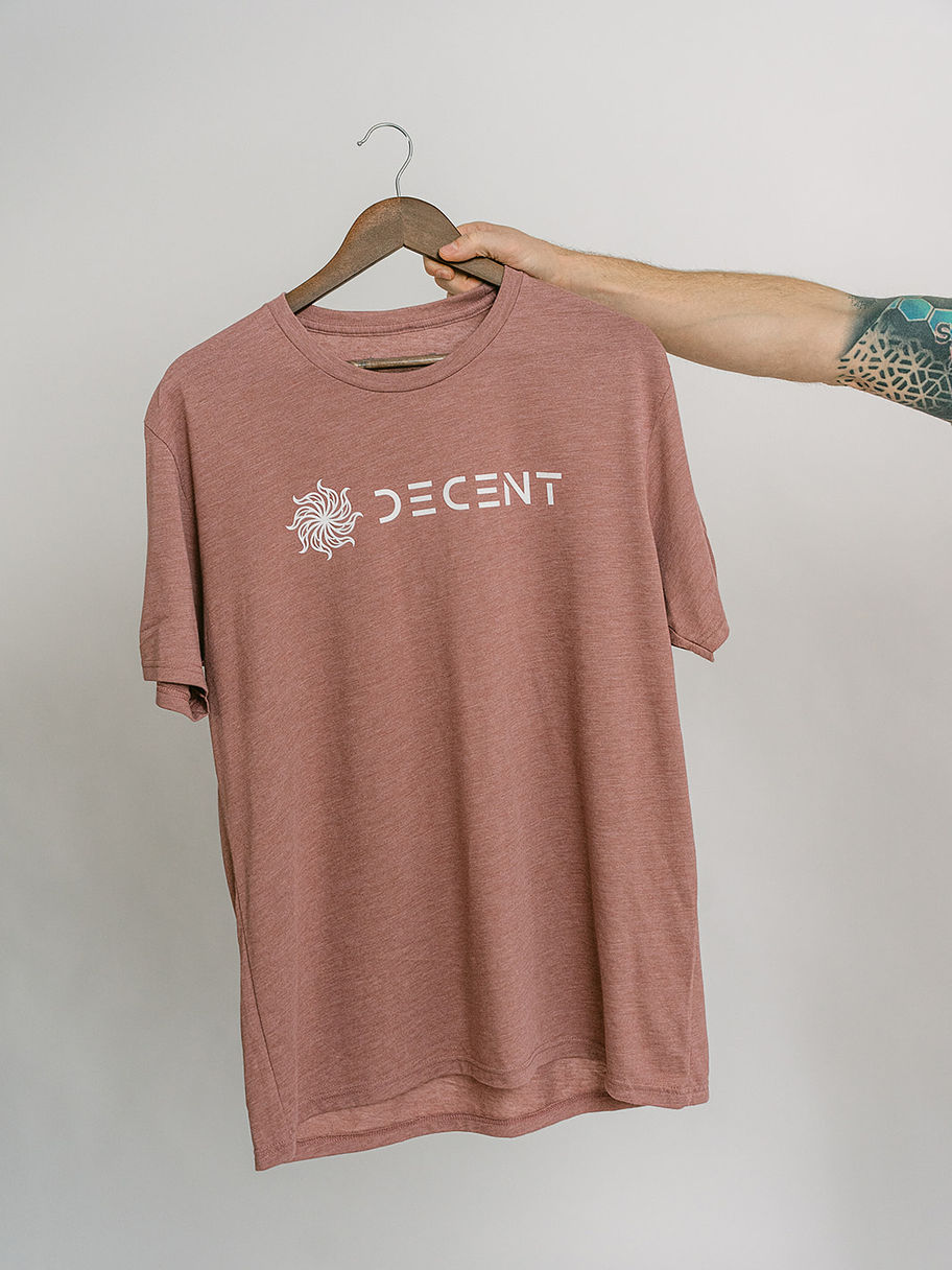 Hand holding up a reddish-brown t-shirt with the Decent Threads logo.