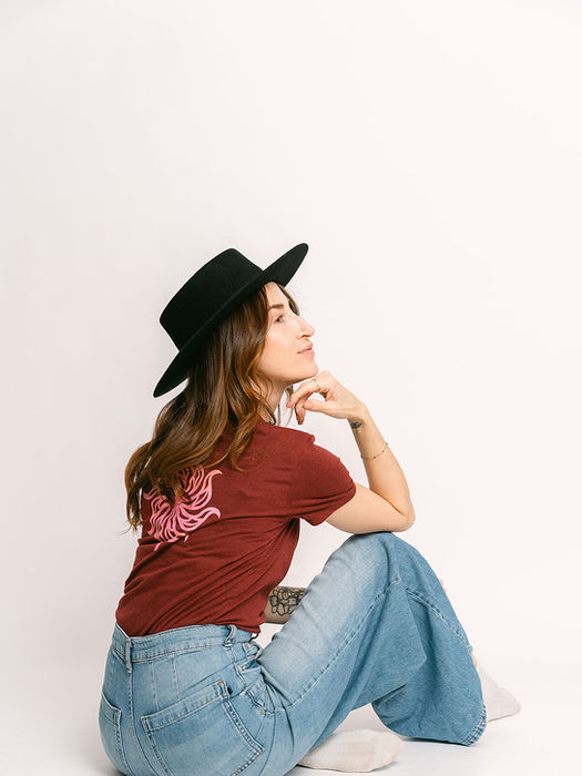 Woman in black hat, maroon Decent Threads tshirt, wide-leg jeans, looking up