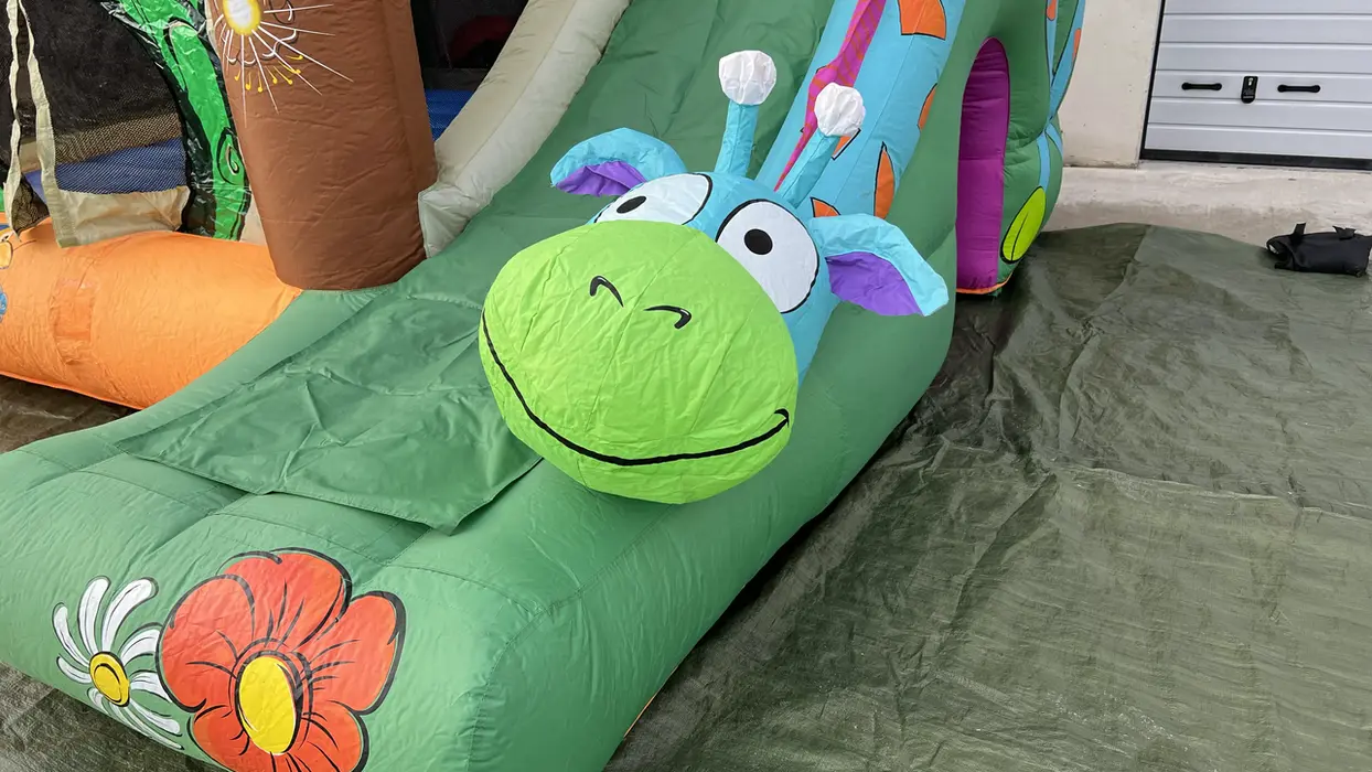 Aufblasbare Rutsche mit lachendem Giraffenkopf, Teil einer bunten Hüpfburg.