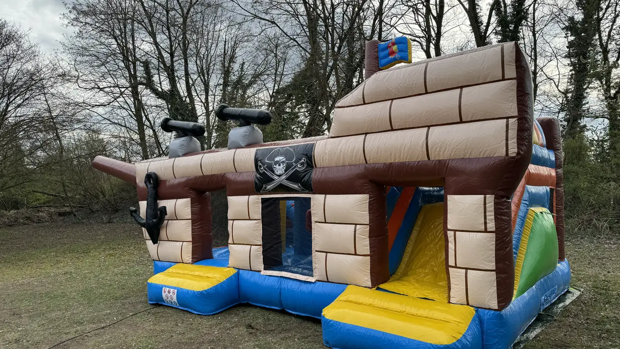 Große aufblasbare Hüpfburg Piratenschiff auf grünem Gras unter Bäumen.