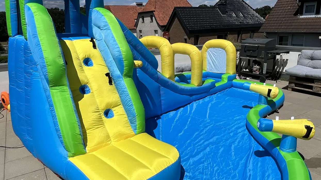 Bunte aufblasbare Wasserrutsche mit Pool unter blauem Sommerhimmel.