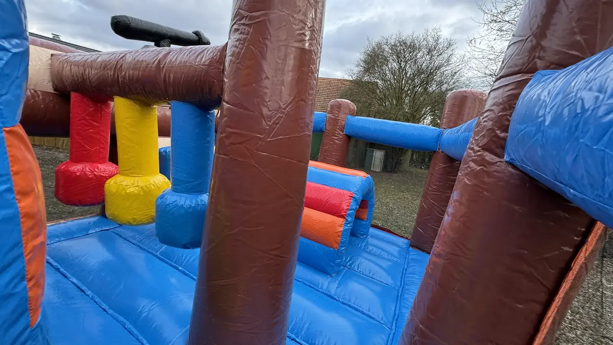 Bunte aufblasbare Hüpfburg mit Hindernissen, blauen Wänden und braunen Säulen.