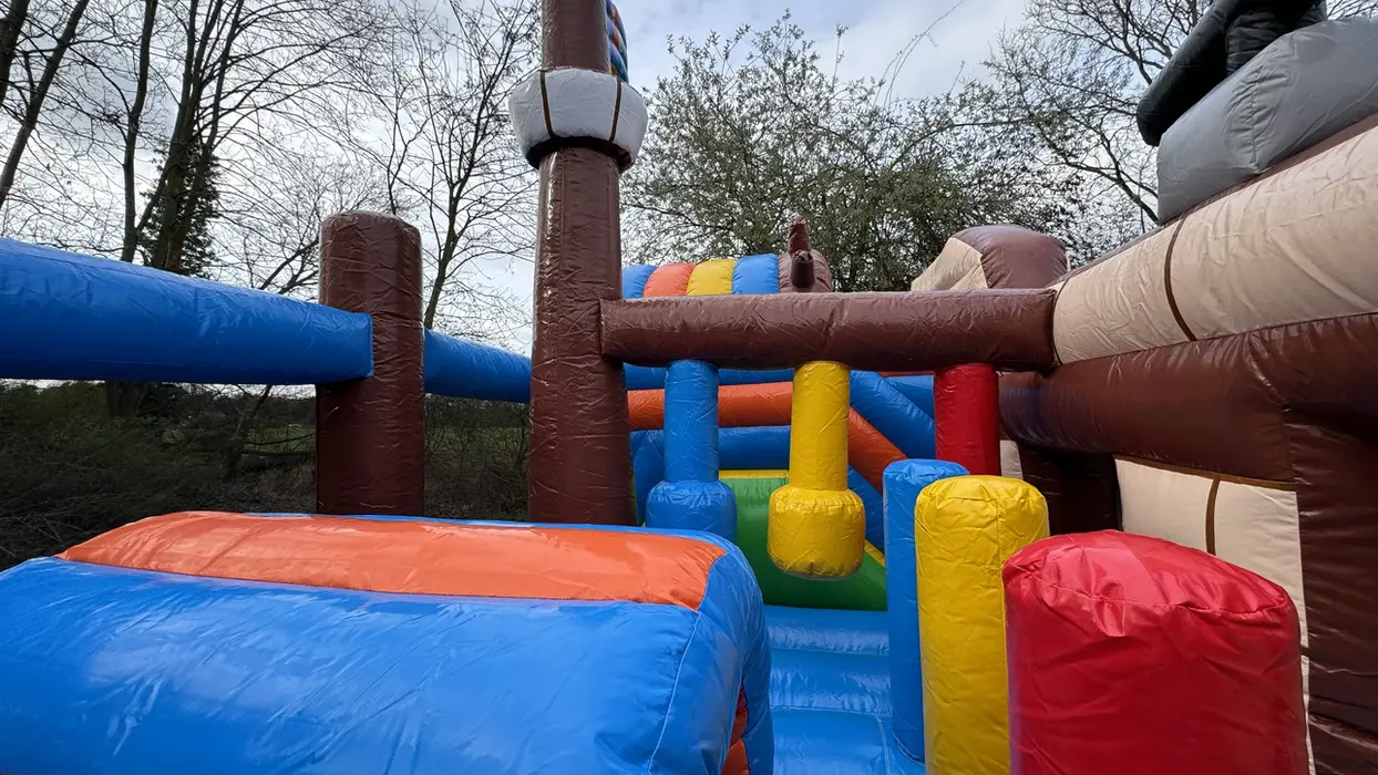 Farbenfroher aufblasbarer Hindernisparcours für Kinder unter Bäumen.