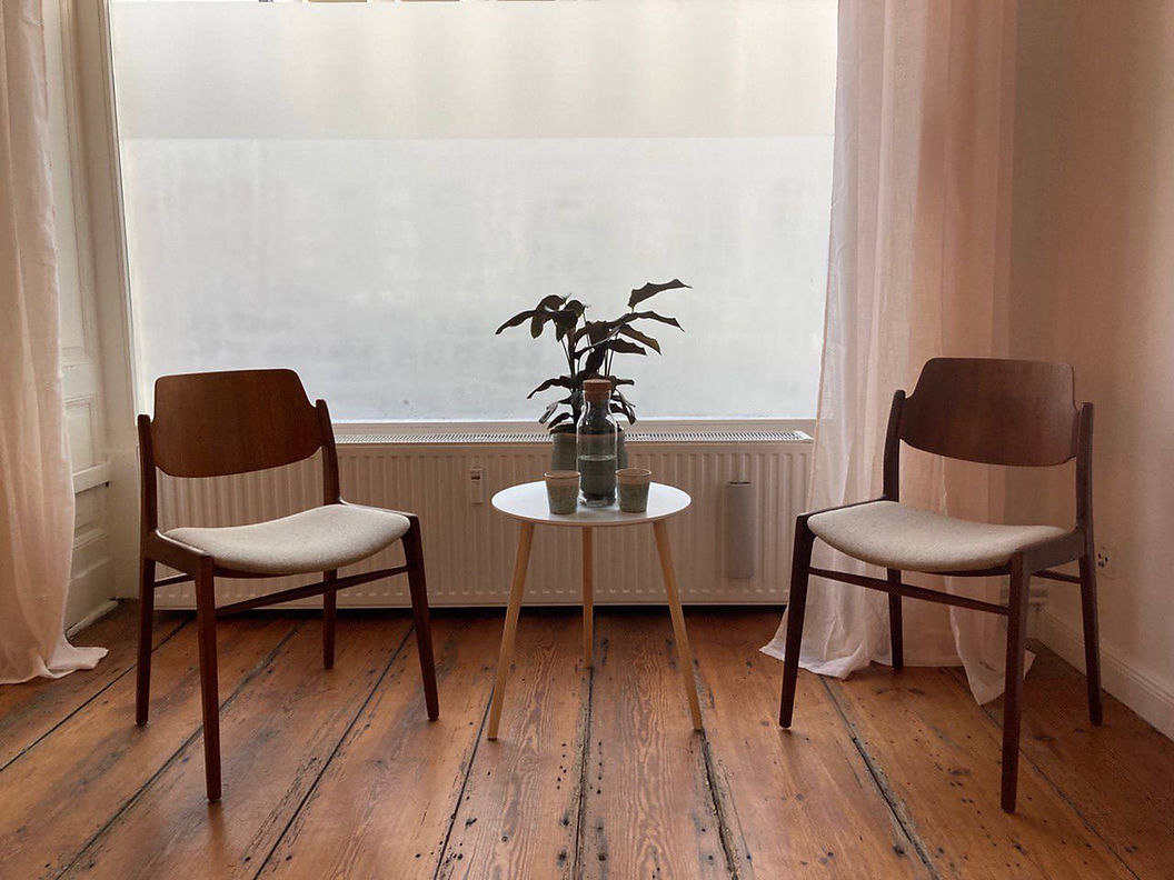 Zwei Holzstühle mit einem Tisch und Pflanze vor einem Fenster.