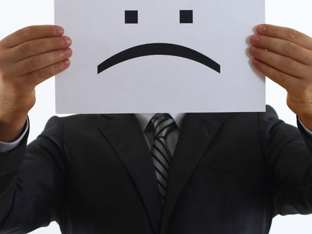 Personal Grievance. Auckland, Wellington, Christchurch. Man in suit holding frowning face in front of head.