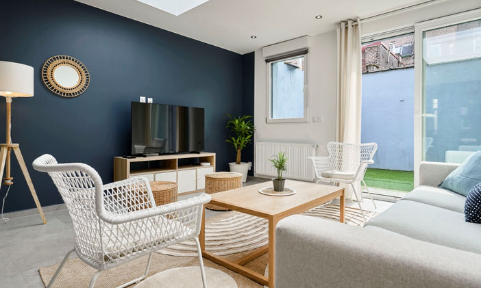 Dans le séjour de cette colocation, les couleurs sont claires et neutres avec un mur bleu marine en mur d'accent. Cpoté matériaux, du bois et des fibres naturelles.