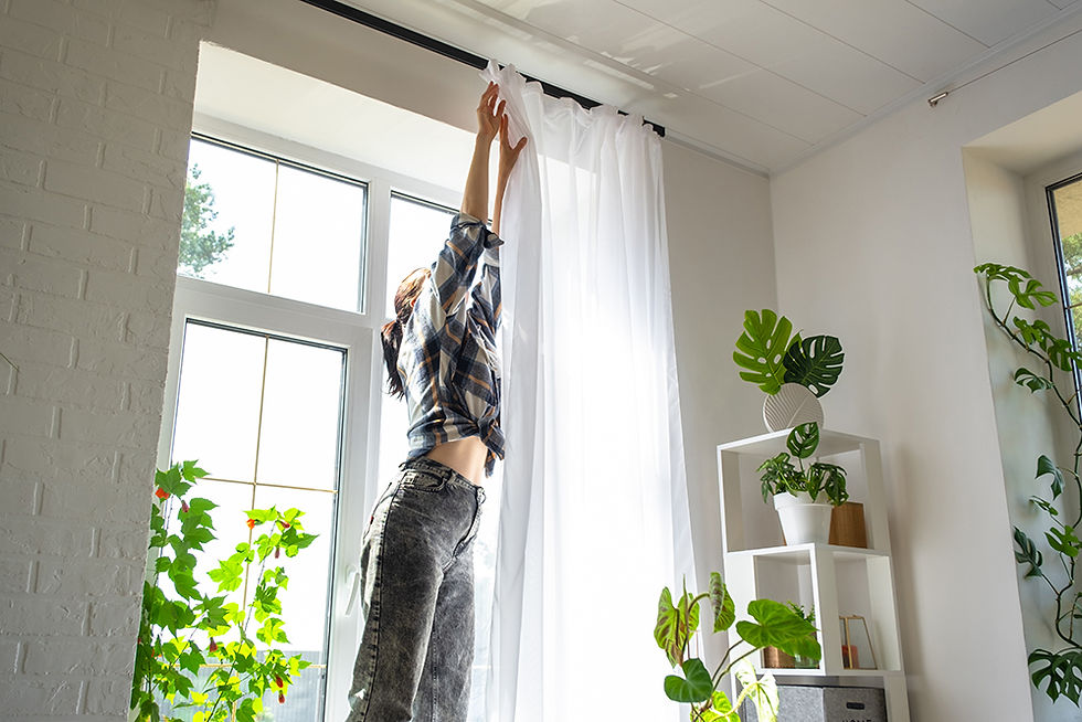 Woman hanging transparent tulle curtains in a bright room, allowing fresh air and sunlight to filter through.