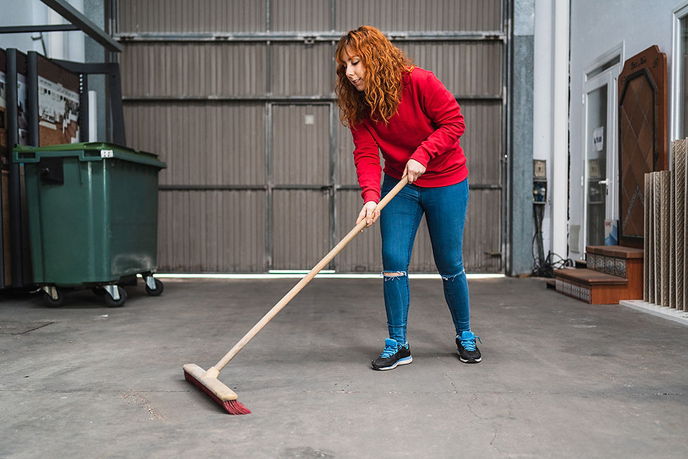 Woman sweeping a garage floor with a large broom, removing dust and debris to reduce allergens.