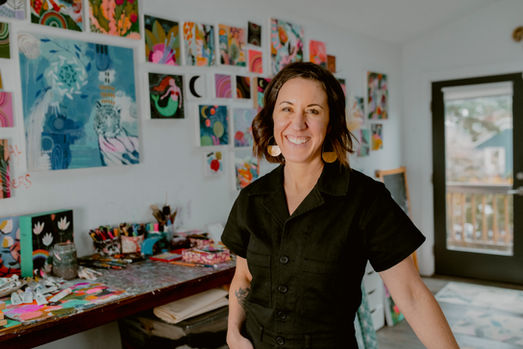 Portrait of artist Jessica Swift in her home studio, standing in front of her paintings.