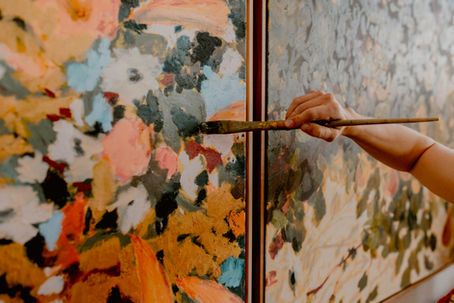 Close up of oil painter adding finishing touches to vibrant, floral paintings.