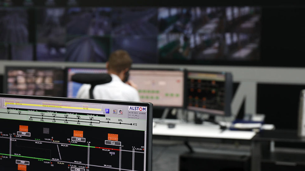 Mężczyzna siedzi przed wieloma monitorami w centrum sterowania metra w Maladze. Ekrany przedstawiają różne dane kolejowe, w tym układy torów, pozycje pociągów i informacje sygnalizacyjne. Logo firmy Alstom jest widoczne w prawym górnym rogu jednego z monitorów.