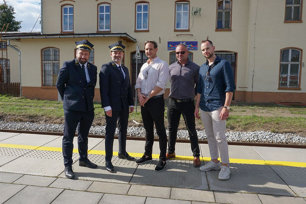 Uroczyste odsłonięcie pamiątkowej tablicy na dworcu w Czaplinku. Na peronie, na tle budynku dworca stoi pięciu mężczyzn. Dwaj z nich, po lewej stronie, ubrani są w mundury kolejowe, natomiast trzej pozostali w ubrania cywilne. Wszyscy pozują do zdjęcia, uśmiechając się.