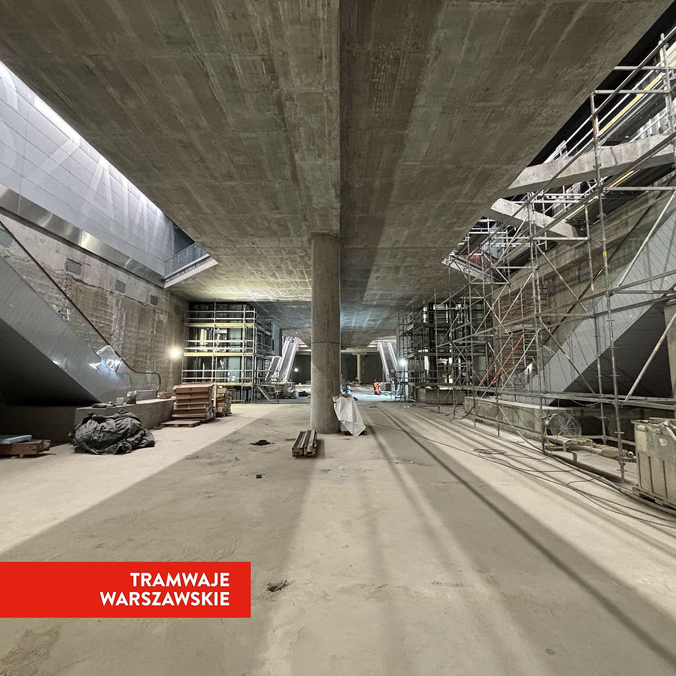 Zdjęcie przedstawia zaawansowany etap budowy podziemnego przystanku tramwajowego, z widocznymi betonowymi konstrukcjami, kolumnami, a także rusztowaniami i częściowo zainstalowanymi schodami ruchomymi. W tle widać wejścia do tuneli.