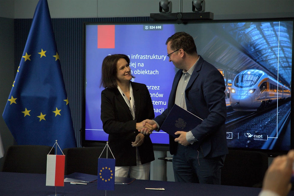 Joanna Lech, dyrektor Centrum Unijnych Projektów Transportowych, i Marcin Mochocki, członek zarządu PKP Polskich Linii Kolejowych, uściskają sobie dłonie, symbolizując pomyślne podpisanie umowy. W tle widoczny jest ekran prezentujący logo CUPT, a na stole znajdują się małe flagi Polski i Unii Europejskiej.
