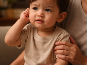 Toddler tugging at ear showing signs of ear infection, sitting on parent lap in Singapore home
