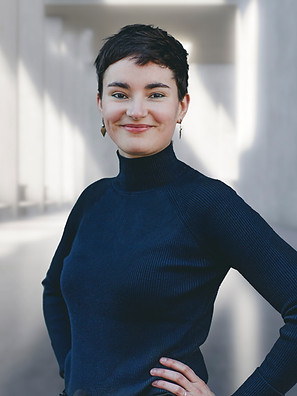 Smiling woman in blue turtleneck poses confidently, ihr Name ist Toni Marie Leisz