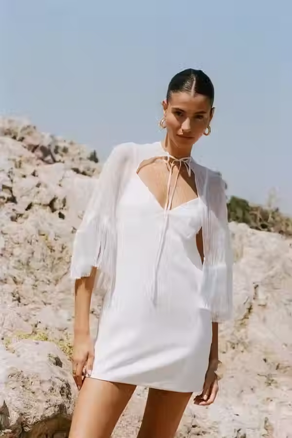 White mini dress with a sleek silhouette and dramatic cape detail for a modern engagement party look.