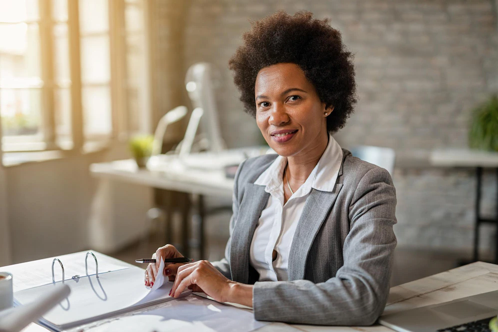 black-smiling-businesswoman-analyzing-financial-reports-while-working-office-looking-camer