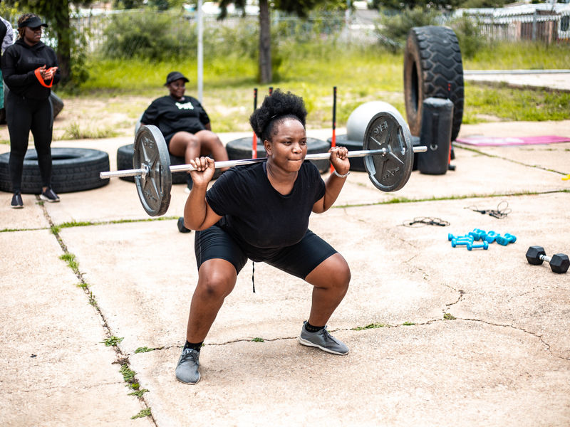A member performing a barbell squat outdoors