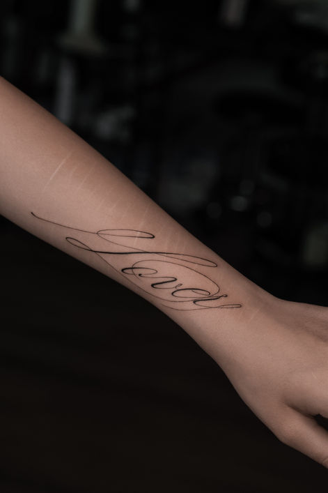 Fine line script lettering tattoo along the inner forearm