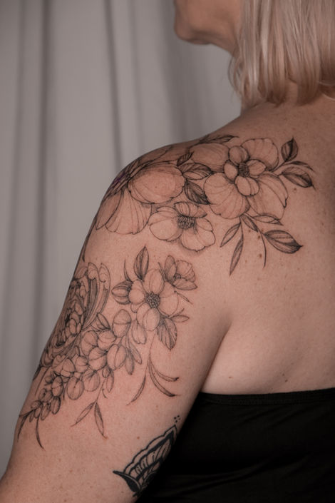 Fine line floral tattoo across the shoulder and upper back with chrysanthemum, peony, anemone and wisteria flowers