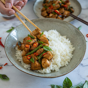 Poulet sauté au basilic thaï servi dans un bol gris sur un lit de riz blanc, morceaux de poulet nappés de sauce brillante et feuilles de basilic frais.
