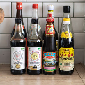 Assortiment des 8 sauces asiatiques indispensables alignées sur un plan de travail : sauce soja claire, sauce soja foncée, huile de sésame, sauce d’huître, sauce de poisson nuoc mam, vinaigre de riz blanc, vinaigre de riz noir et vin de Shaoxing.