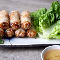 Nems au poulet croustillants servis dans une assiette blanche avec salade verte et feuilles de menthe fraîche, spécialité vietnamienne dorée et appétissante.