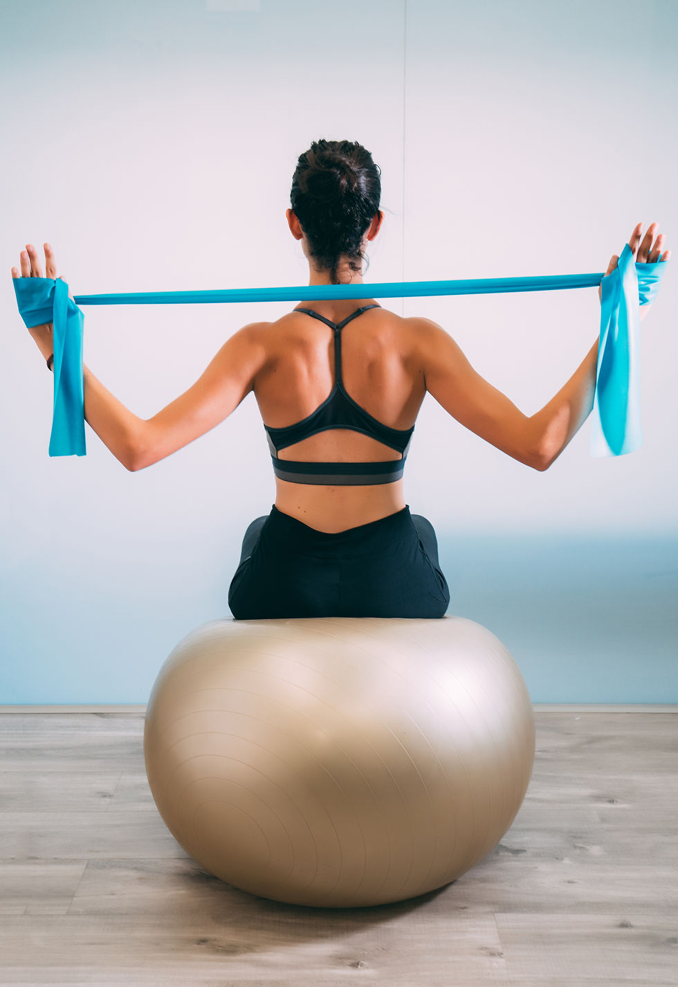 Young sporty attractive woman practicing pilates with resistance bands back sitting on fit