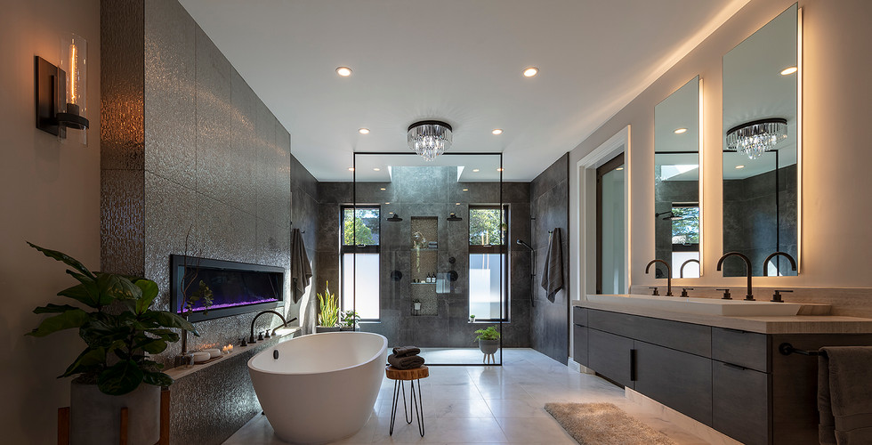 Luxury High-End Modern Bathroom Remodel with a Left Side 12 Inches Thick Brown Mosaic Tiled Accent Fireplace Wall; Left Side Fireplace Front Floor Standing White Bath Tub; Right Side Wall Hung Dark Stained Walnut Wood Floating Drawers and Doors Double Sink Bottom Lit Vanity with an extra large 72 inches Wide Counter Rectangled White Vessel Sink; 2 black counter faucets; Wall Mounted Double 30 inches Wide x 60 inches Height Backlit Mirrors; centered at back wall is a double entry no doors divided by a centered clear glass divider walk-in shower; ceiling recessed can lighting system with 2 centered chandeliers; beige and brown painted walls; white painted ceiling; left side has 2 warm light wall sconces; 1 beige fur rug at the bottom of the vanity; 1 tankless toilet.