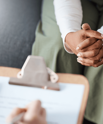 Patient sits with hands clasped while a mental health provider takes notes.
