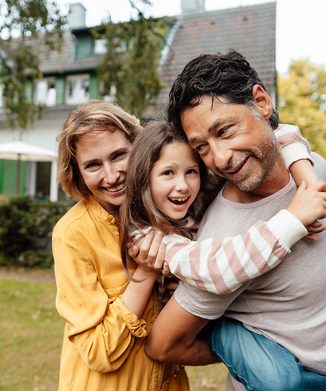 Parents embracing their smiling young child outdoors.