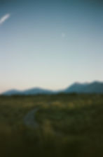 a sunset over a open field with mountains in the background, shot on film